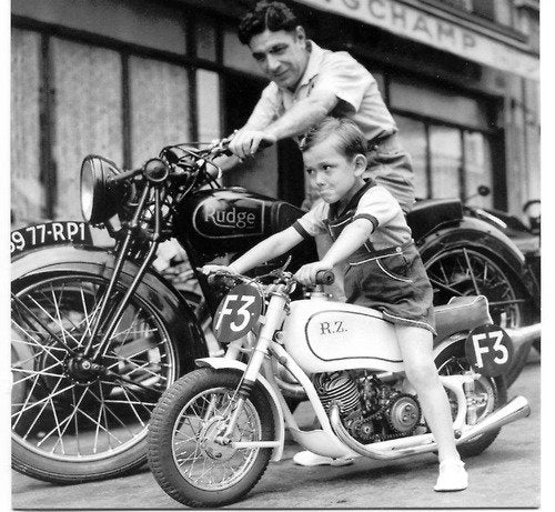 Vintage black and white shot of a boy on a small motorbike beside a man on a Rudge motorcycle