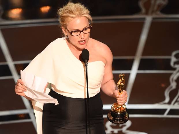 Actress in a white one-shoulder top holding an Oscar statuette and her speech notes at a microphone