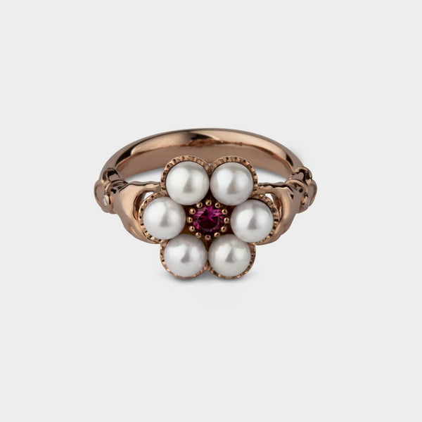 rose gold posy ring seen from the front. The hands on each side of the setting are visible. The ring is round white akoya pearls and a ruby.